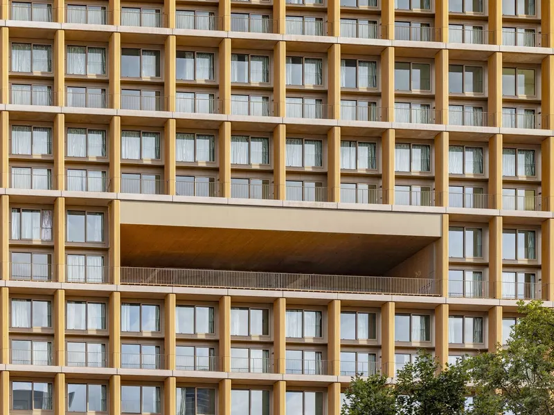 Close-up of timber grid facade with recessed terrace opening and balustrade beneath overcast sky