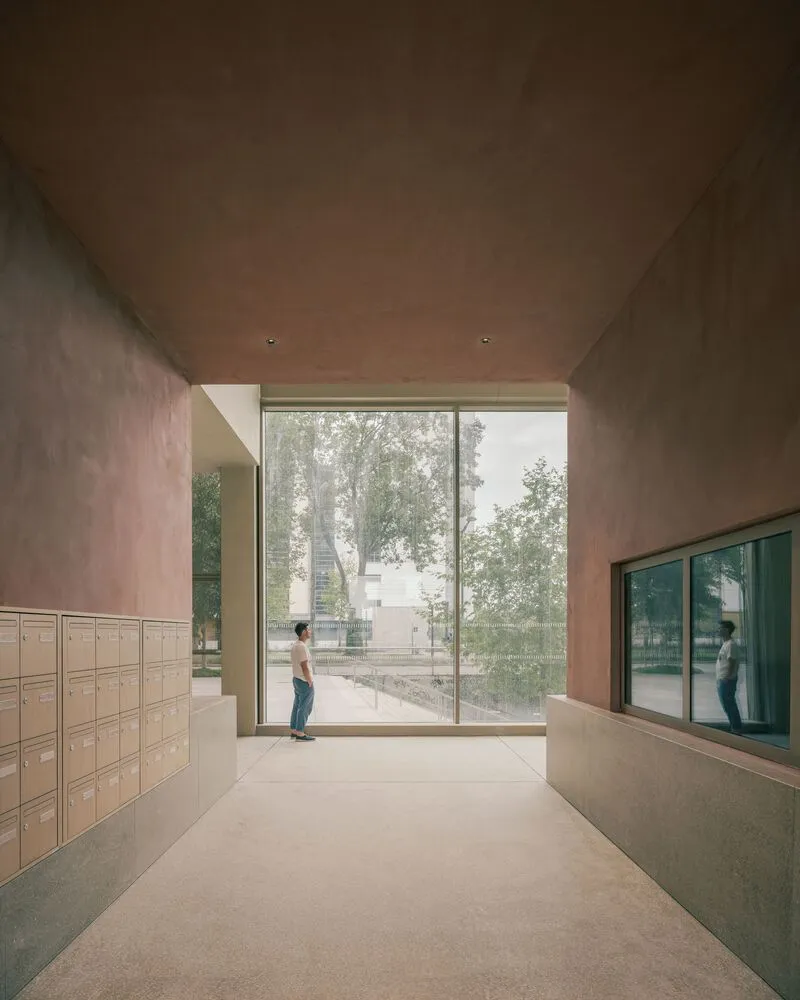 Entry lobby with terrazzo floor, timber mailbox wall, and glazed corner looking toward trees outside