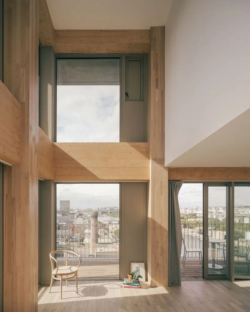 Double-height living space with exposed timber structure and sunlight streaming through floor-to-ceiling windows