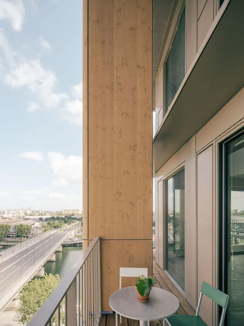 Timber-framed balcony with metal railing overlooking a canal and highway on a sunny afternoon