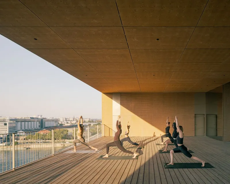 Covered terrace with timber ceiling and decking where three people practice yoga at dawn