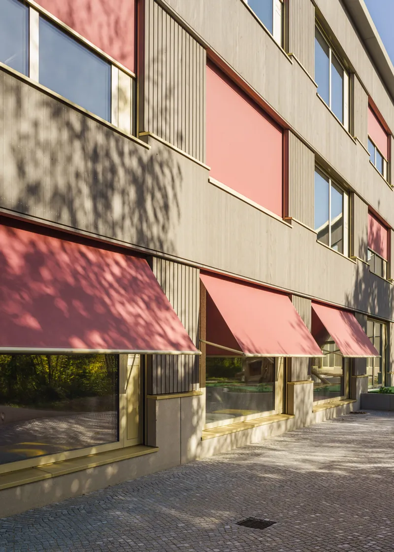 Facade with pink awnings and ribbed panels casting dappled tree shadows in afternoon light