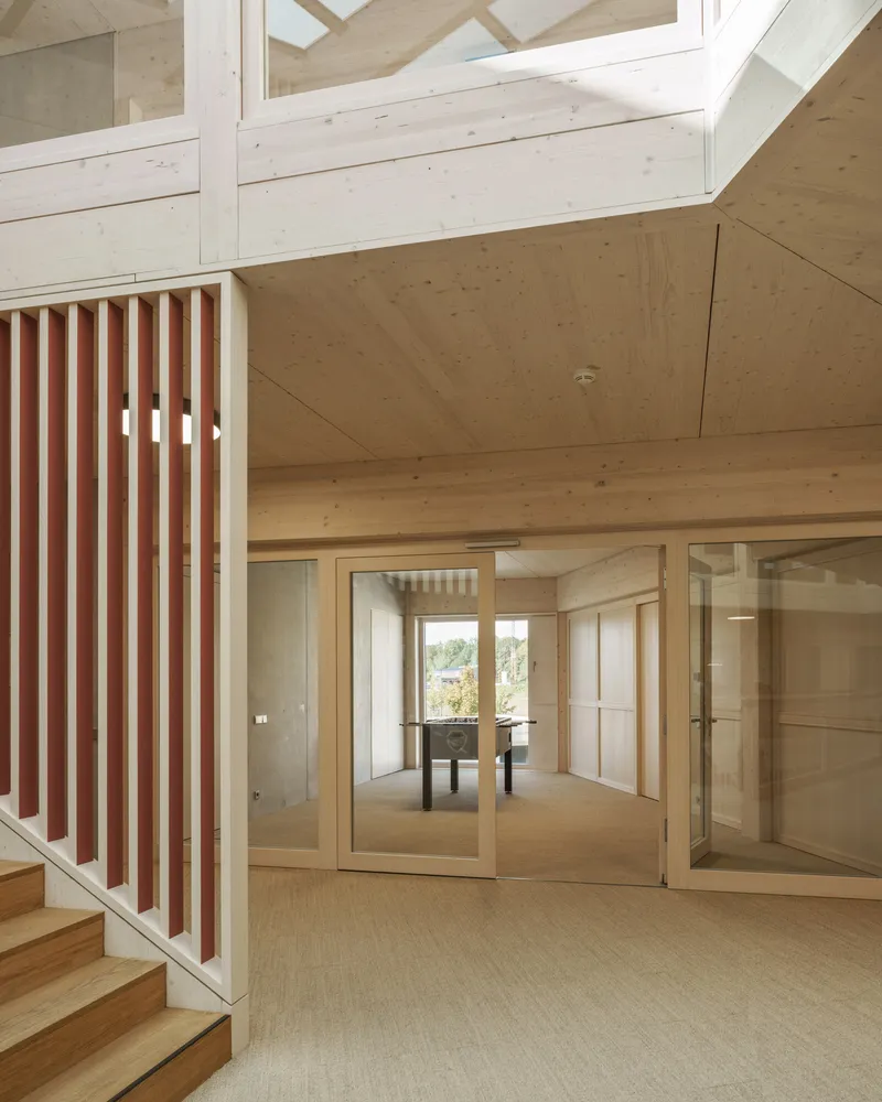 Interior hallway with red-striped balustrade and glazed walls looking into a meeting room