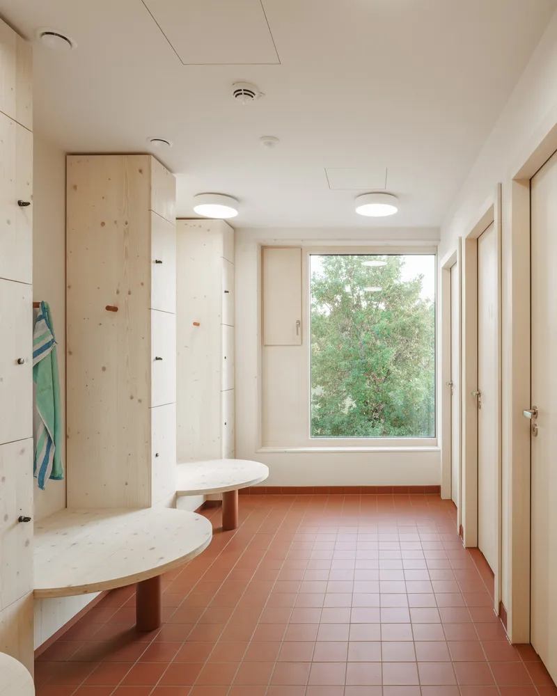 Entrance hall with terracotta tile floor, plywood storage cabinets and window framing green foliage outside