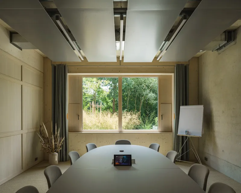Conference room with oval table and ceiling-mounted linear lighting framing window view to meadow