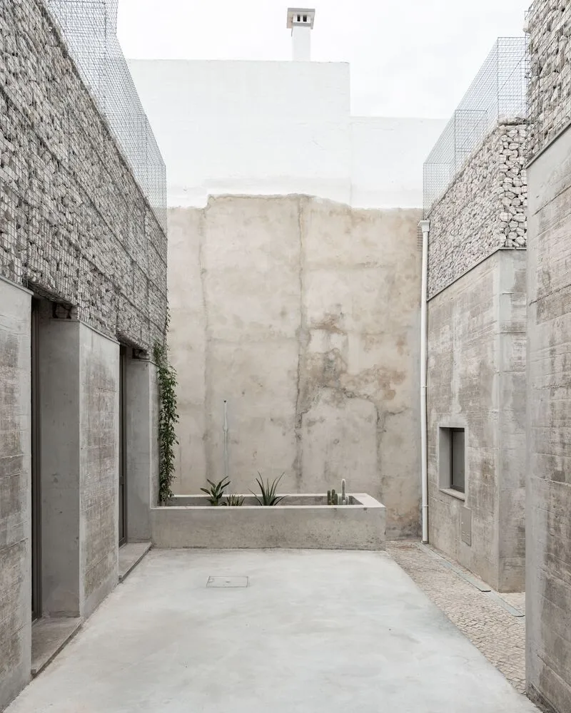 Concrete courtyard with planted bed and stone gabion walls rising on either side