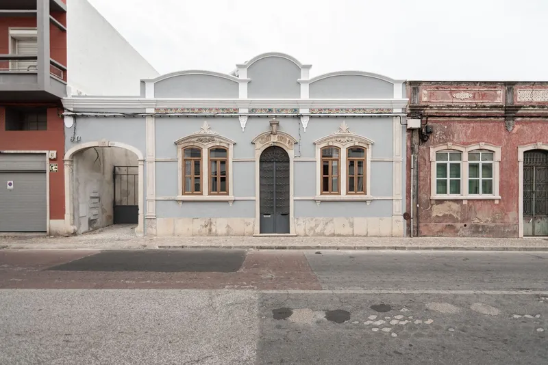Street view of three adjacent facades with arched parapets and ornamental window surrounds under overcast sky