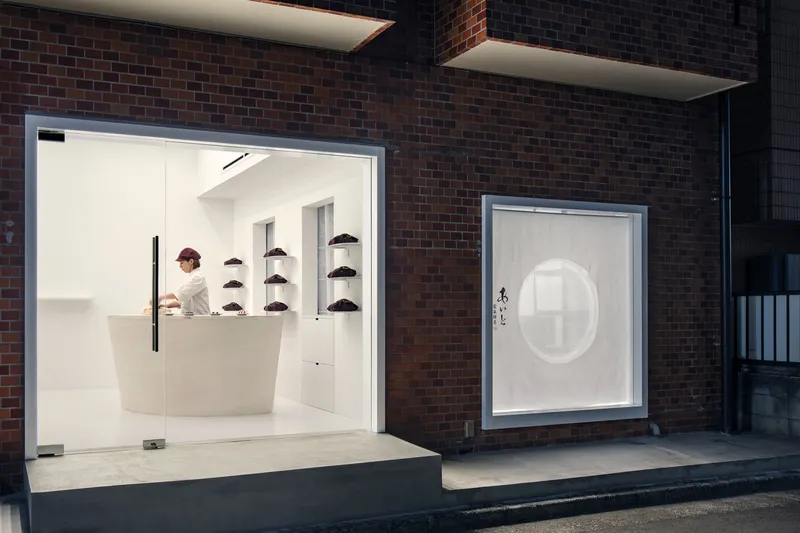 Evening view of illuminated shopfront with curved counter and circular window in dark brick facade