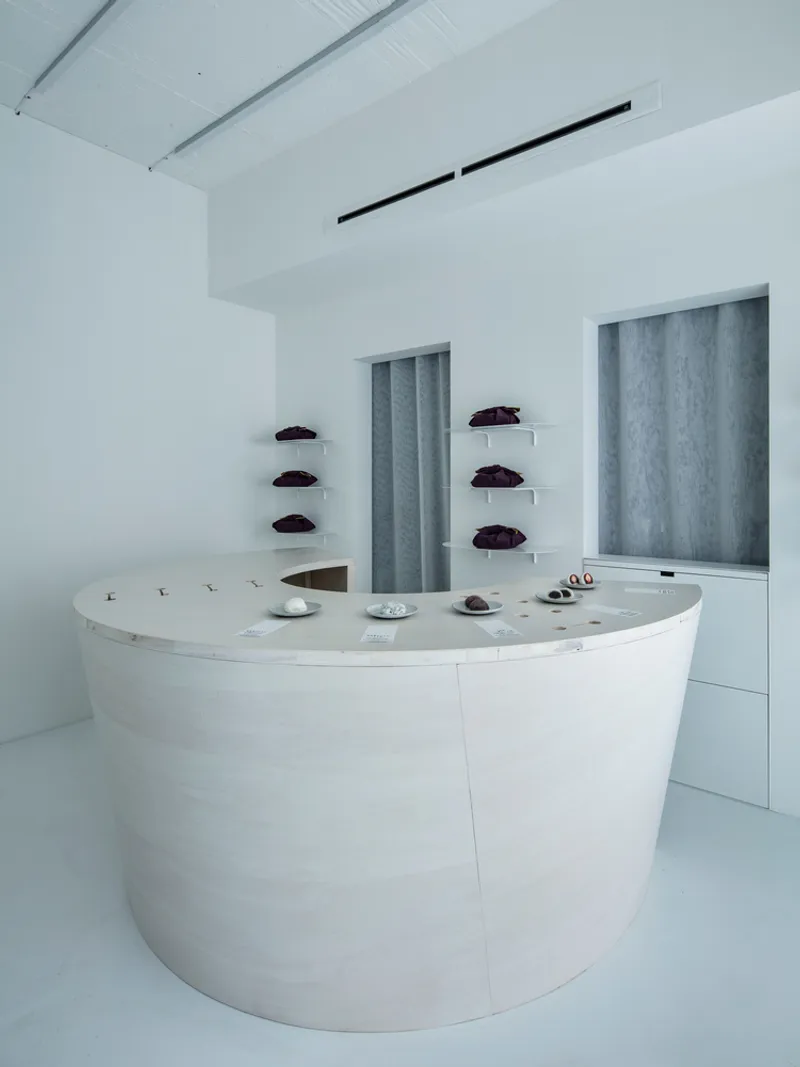White cylindrical display counter with floating shelves behind grey fabric panels in a minimalist retail interior