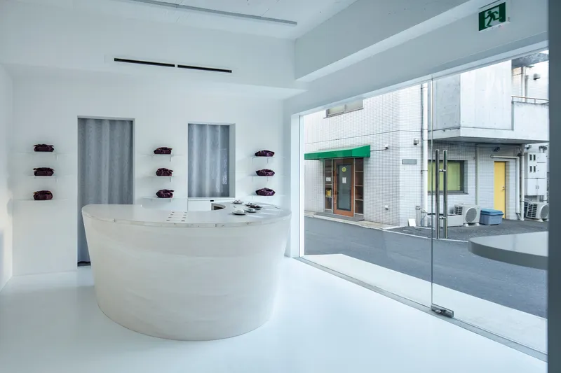 Shopfront glazing revealing white interior counter and view to tiled street facade across the lane