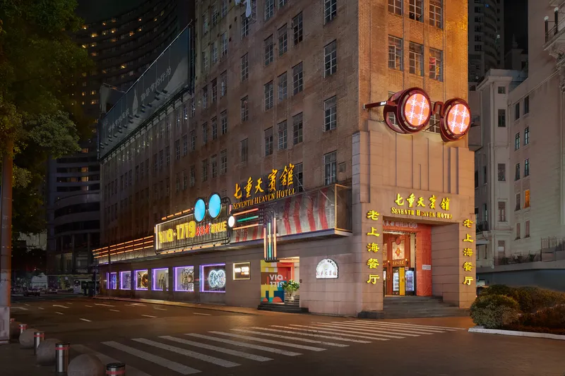 Street view of illuminated hotel entrance with neon signage and large circular light fixtures at dusk