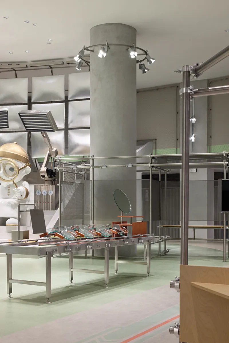 Concrete column with spotlight ring beside steel conveyor framework and white robotic display on mint epoxy floor