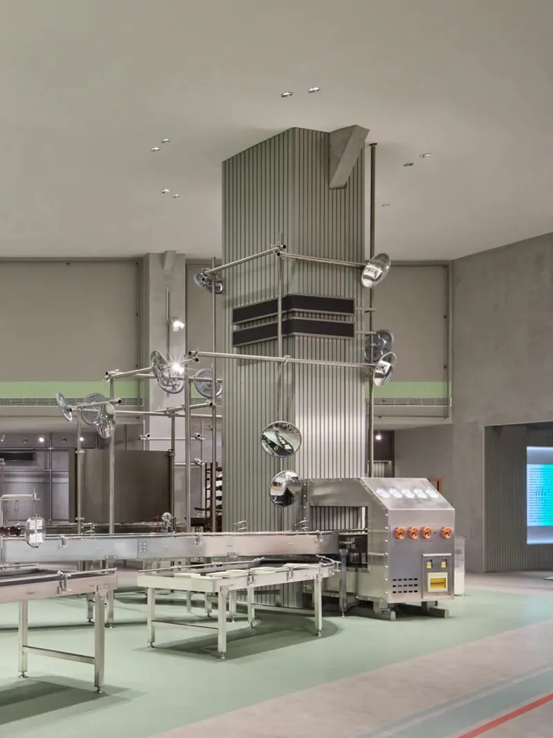 Ribbed tower element with horizontal metal louvers flanked by conveyor systems and equipment under recessed ceiling lights