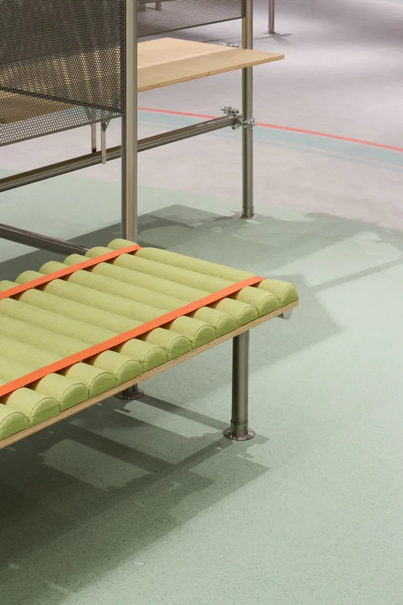 Tubular yellow bench with orange straps on pale green flooring beside steel railings and mesh partitions