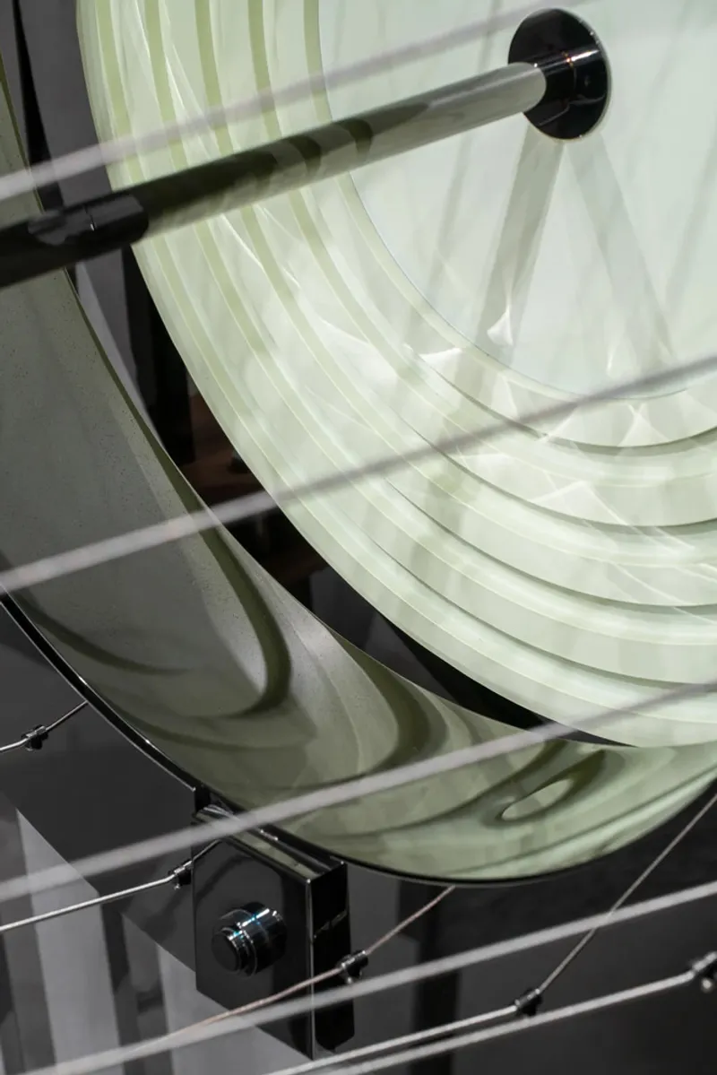 Curved translucent fabric panels suspended by steel cables creating layered shadows on a reflective surface