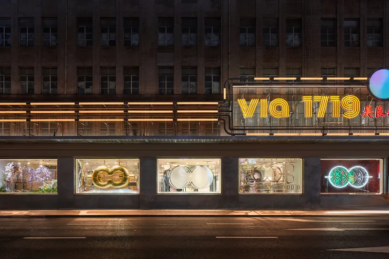 Illuminated storefront with neon signage and framed display windows beneath a striped brick facade at night