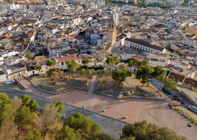 Aerial view of a triangular plaza with brick paving and scattered trees at the edge of a dense urban fabric