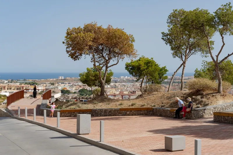 Public plaza with concrete bollards and stone benches under umbrella pines overlooking the townscape below