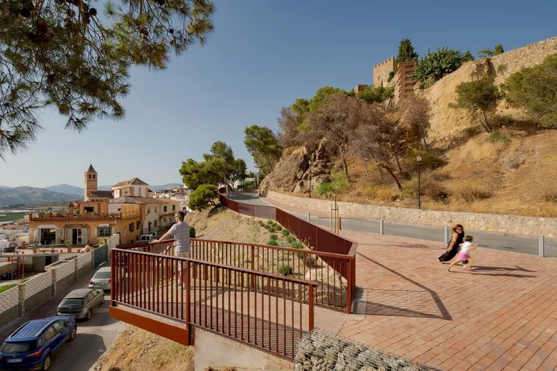 Pedestrian ramp with vertical metal railings connecting levels of the brick terrace as children play