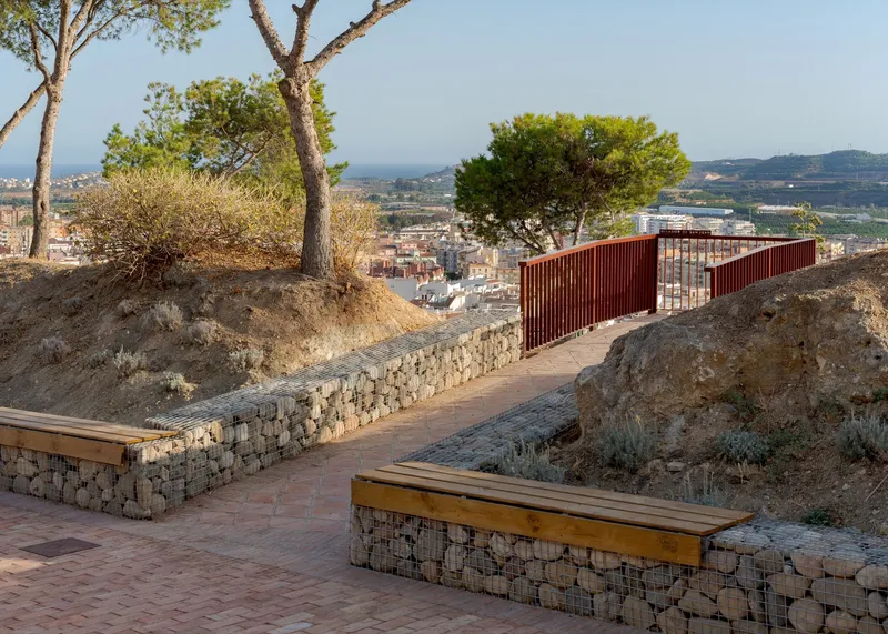 Gabion-clad bench and retaining walls integrating the hillside topography with timber seating and metal screens