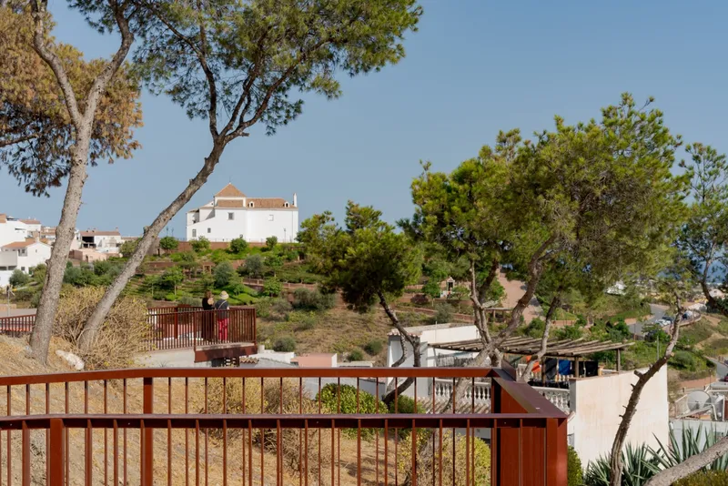 Red metal railing with vertical slats curving along a hillside pathway framed by pine trees