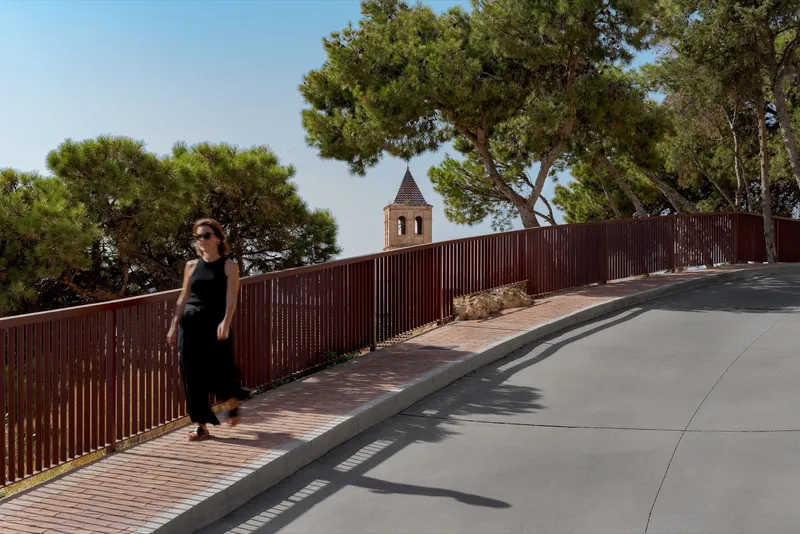 Woman walking on split pathway with red metal railing and terracotta paving in midday sun