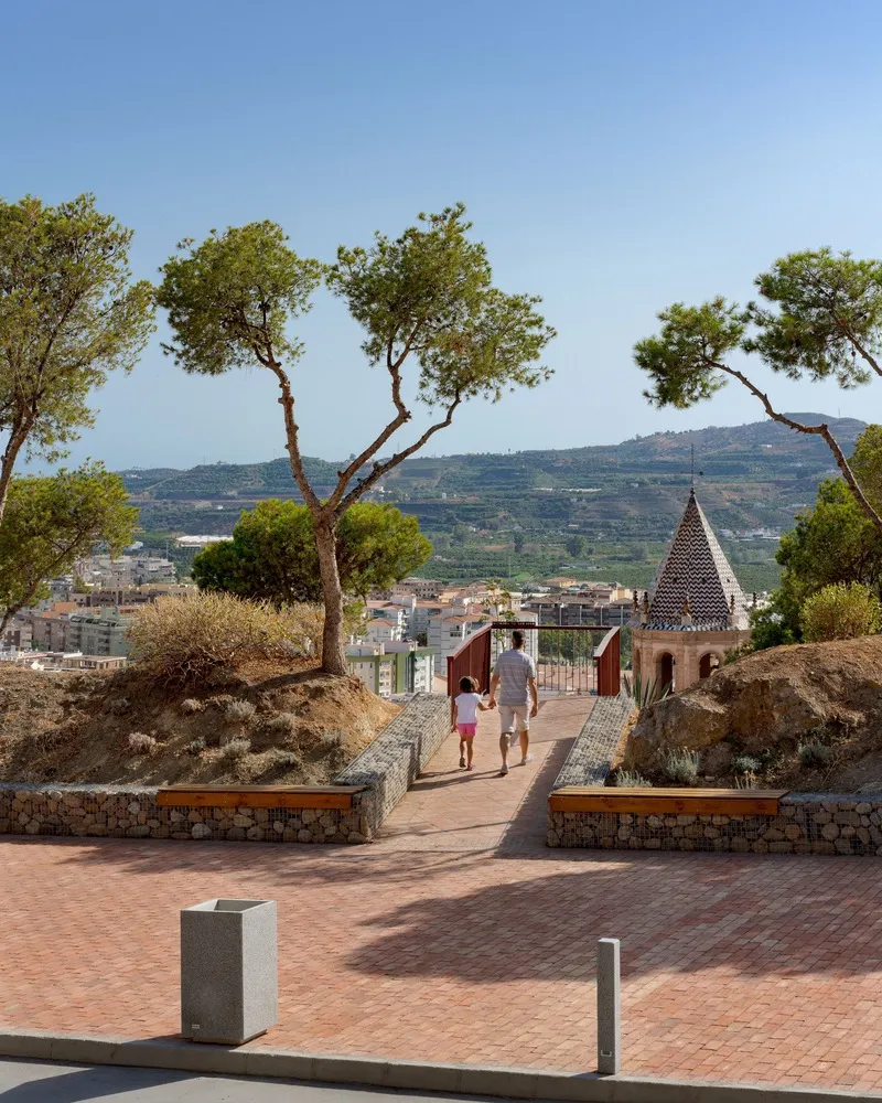 Paved terrace with planted beds in stone walls framing a walking path as visitors approach the tower