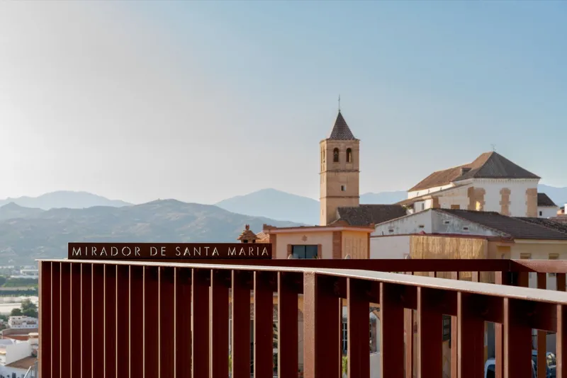 Vertical timber slat facade of the viewpoint structure with the historic church tower rising beyond at dusk