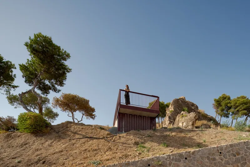 Steel observation deck with perforated facade perched on a rocky hillside among windswept pine trees