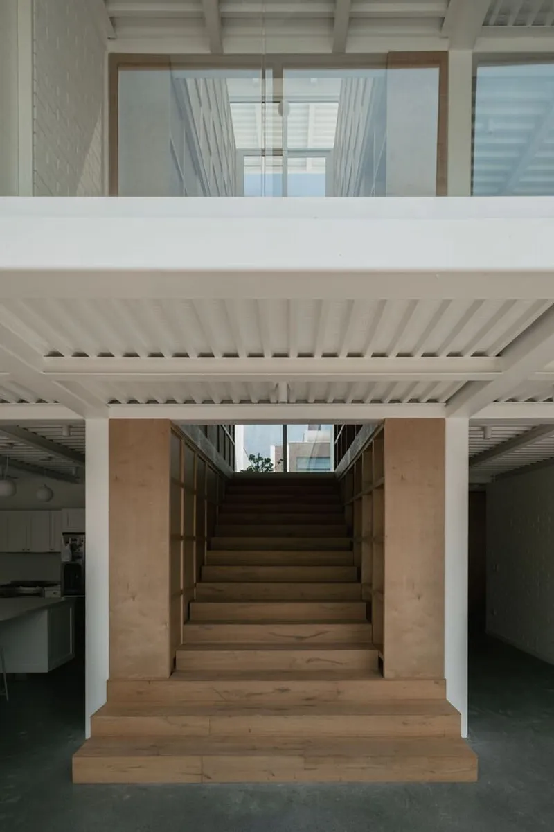 Timber staircase framed by white slatted ceiling beams leading up to a skylit opening above