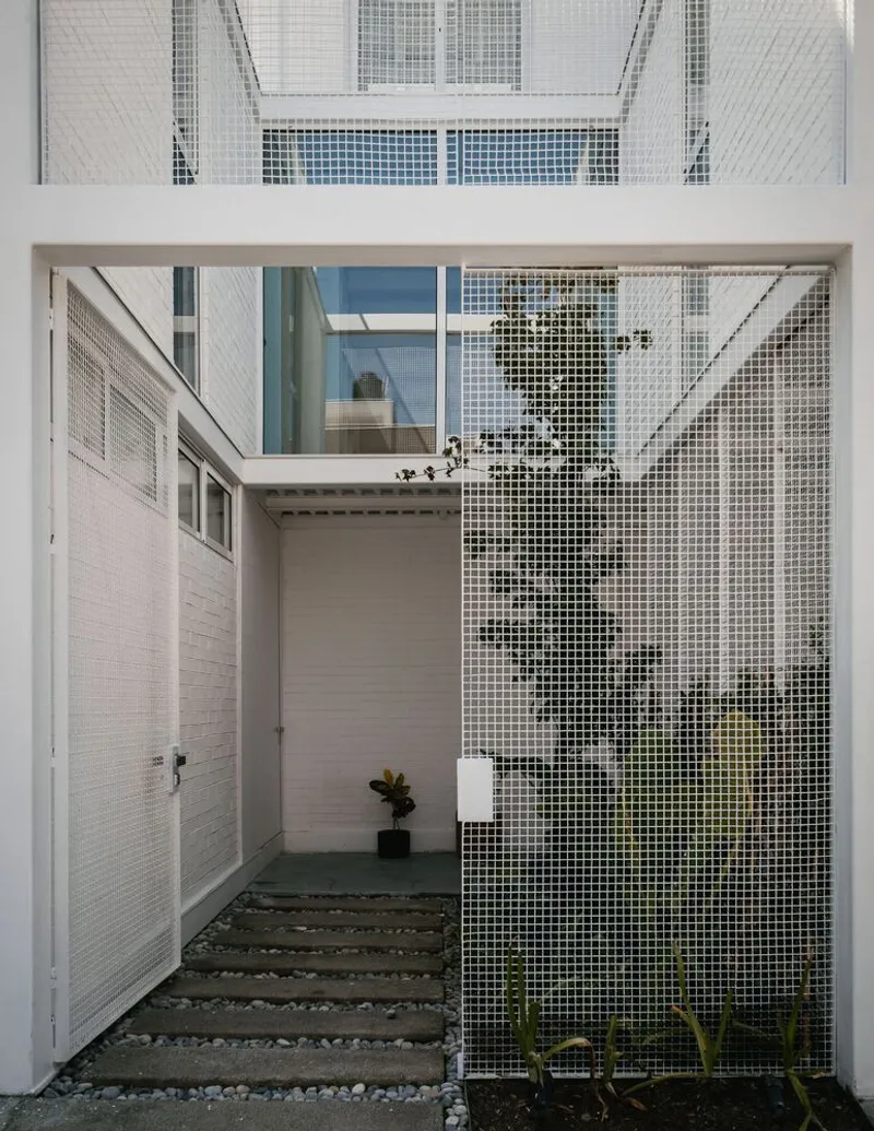 Courtyard entry with concrete stepping stones on gravel leading to a perforated metal screen wall