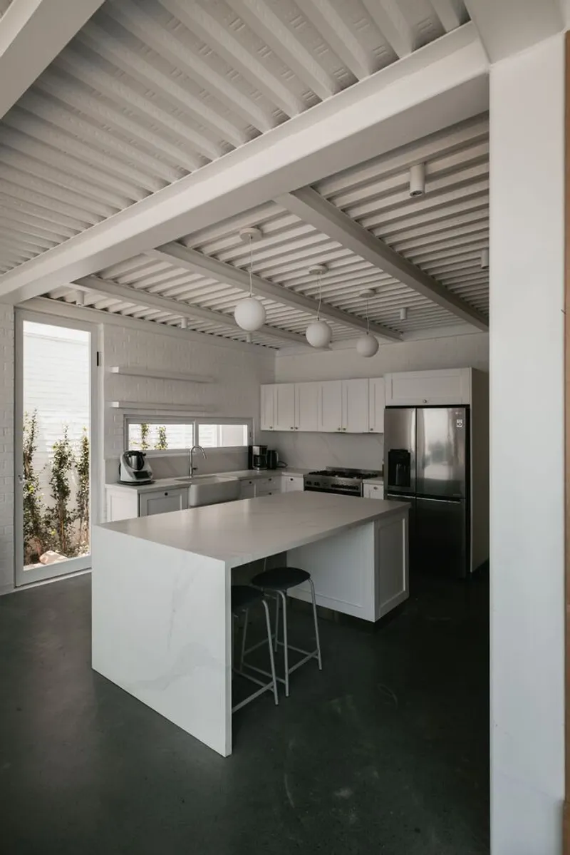 Kitchen with white island and slatted ceiling beams casting shadows across polished concrete floor