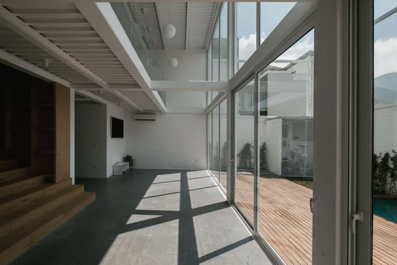 Glass wall opening to timber deck with sunlight casting diagonal shadows on concrete floor