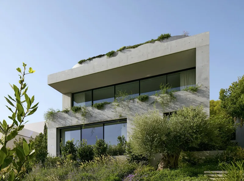 Two-story concrete facade with cantilevered volumes and planted terraces amid Mediterranean vegetation