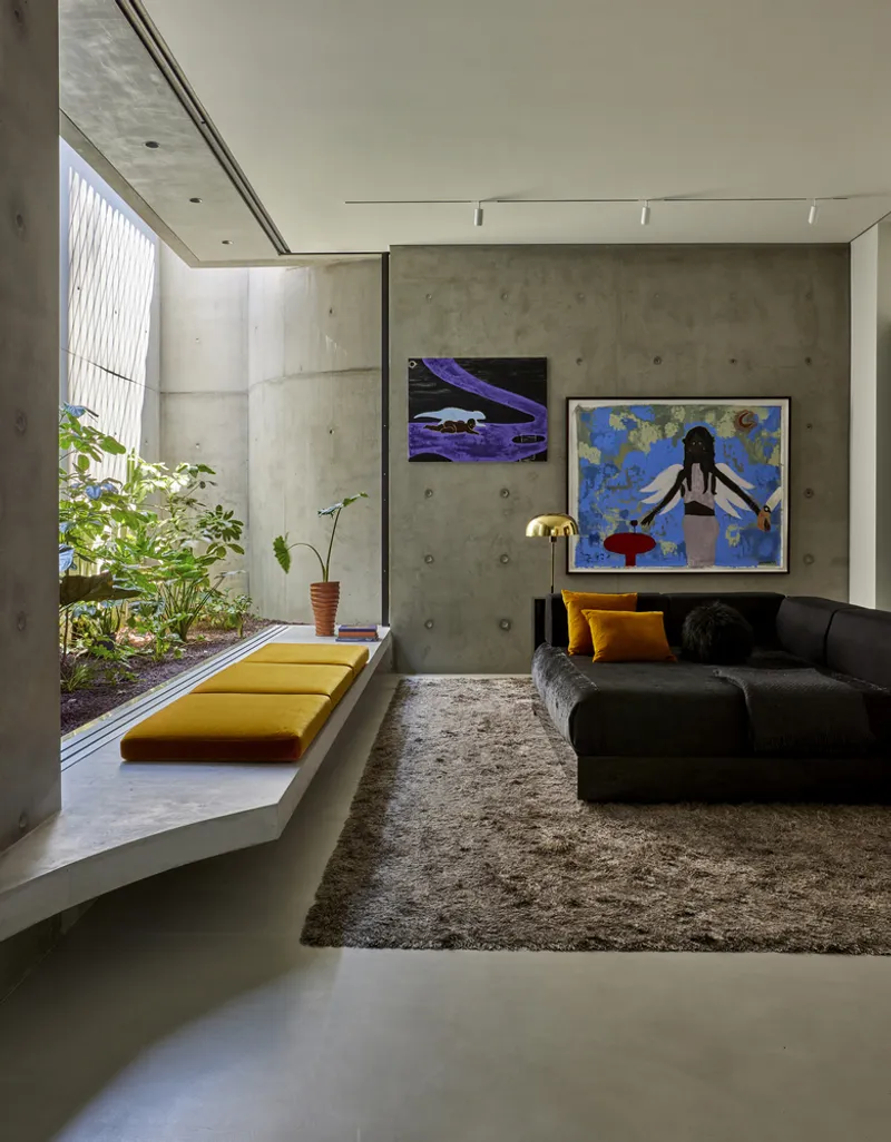 Living room with concrete walls opening to a planted courtyard through a slender glazed slot
