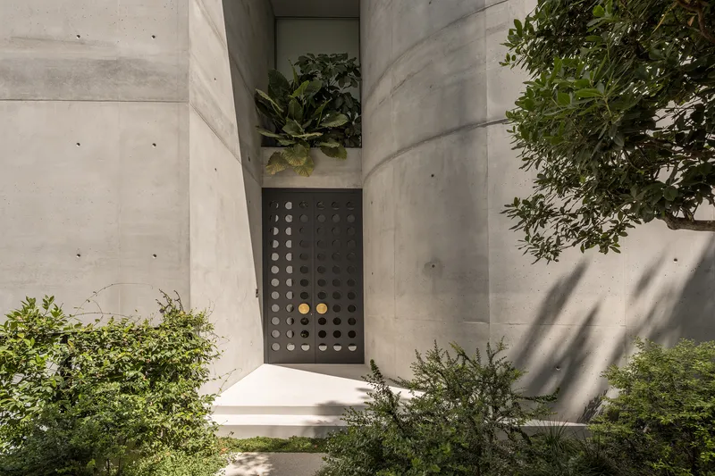 Entry alcove with perforated steel door between board-formed concrete walls casting dappled shadows