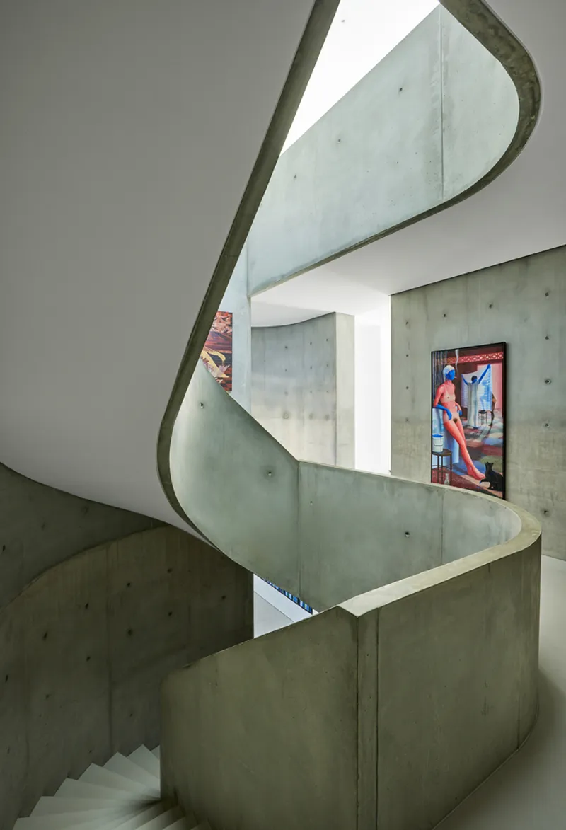 Spiraling concrete staircase rising through three levels with a framed artwork on the landing