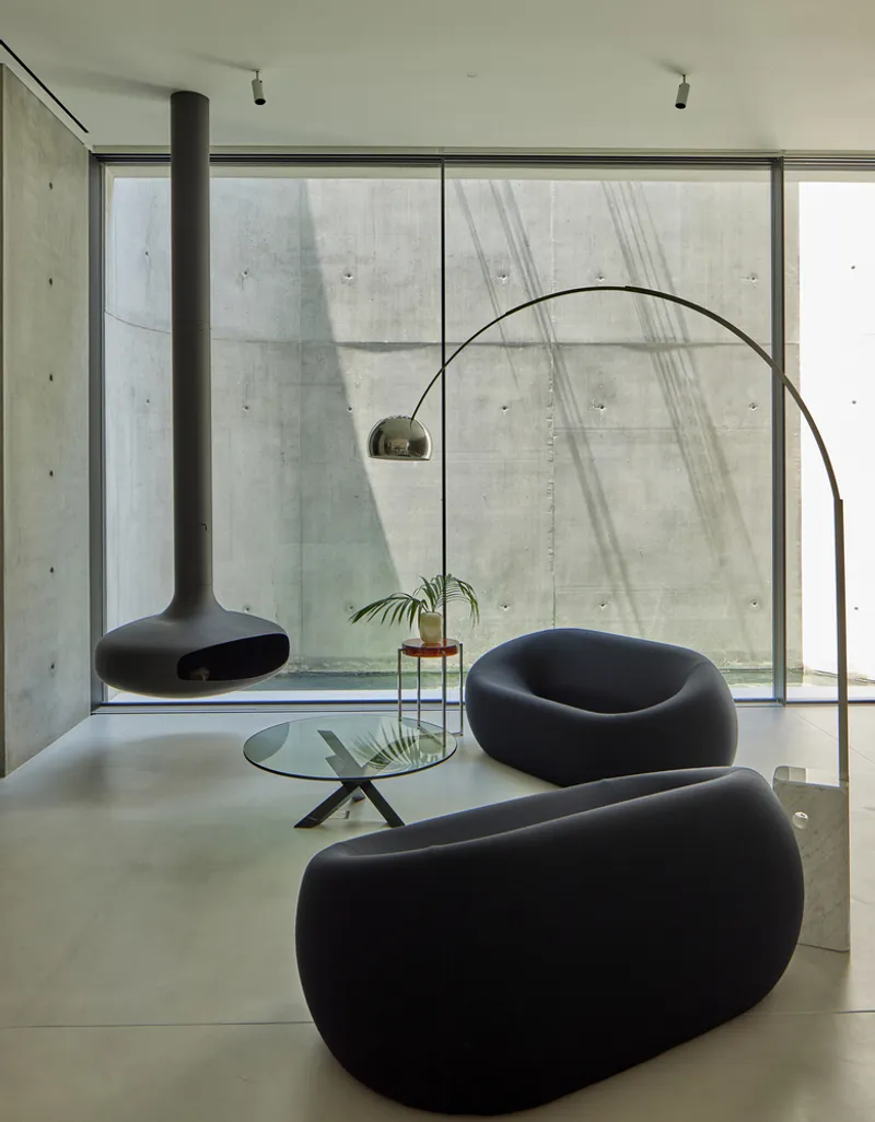 Living area with floor-to-ceiling glazing facing board-formed concrete courtyard wall and suspended black fireplace