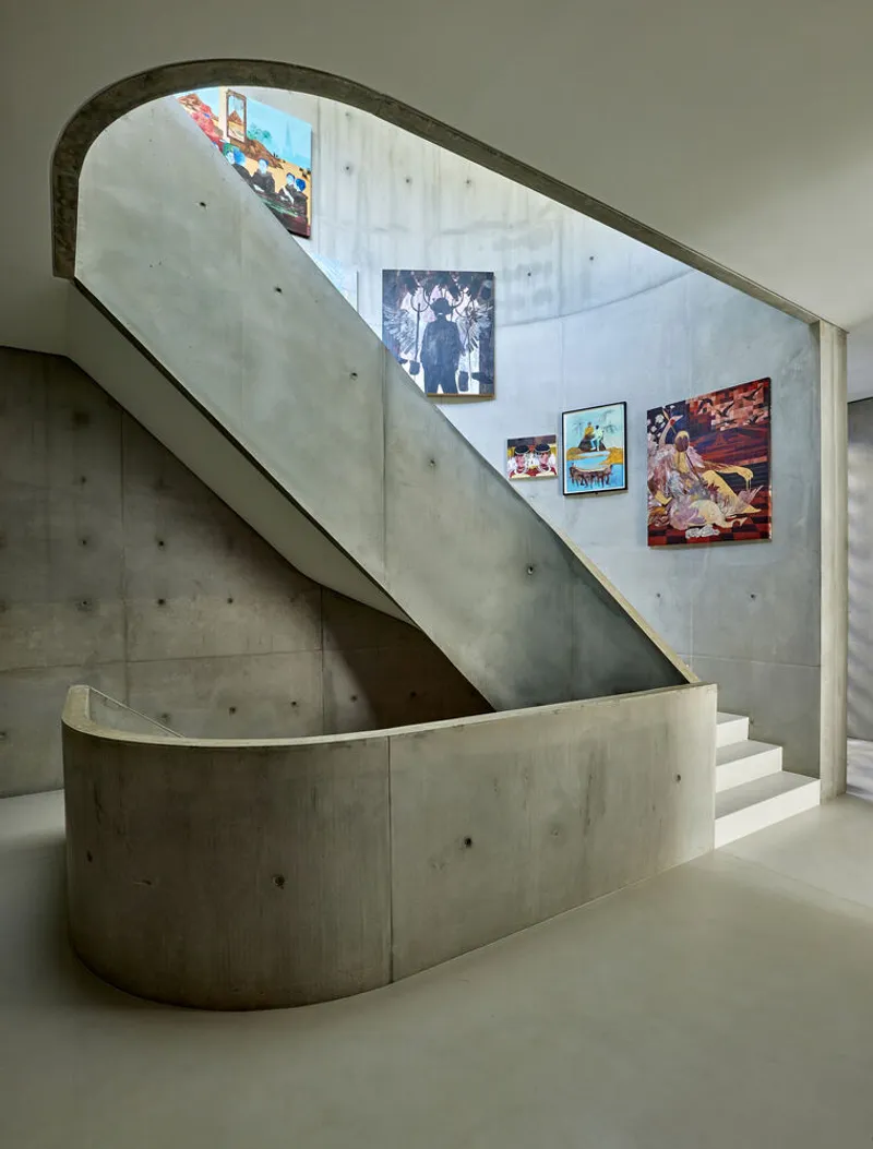 Curved concrete staircase with arched opening and gallery of framed artworks on the wall above