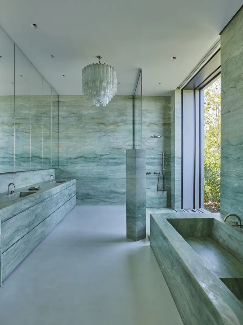 Bathroom interior with mirrored walls and veined marble surfaces under a tiered glass chandelier