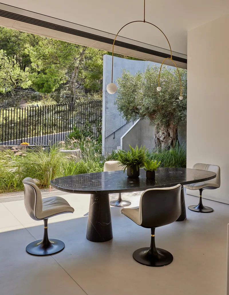 Dining area with a dark marble table and arched pendant light overlooking an olive tree courtyard