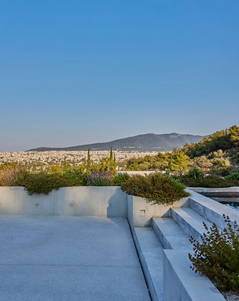 Rooftop terrace with concrete benches and planted edge overlooking a distant mountain and city below