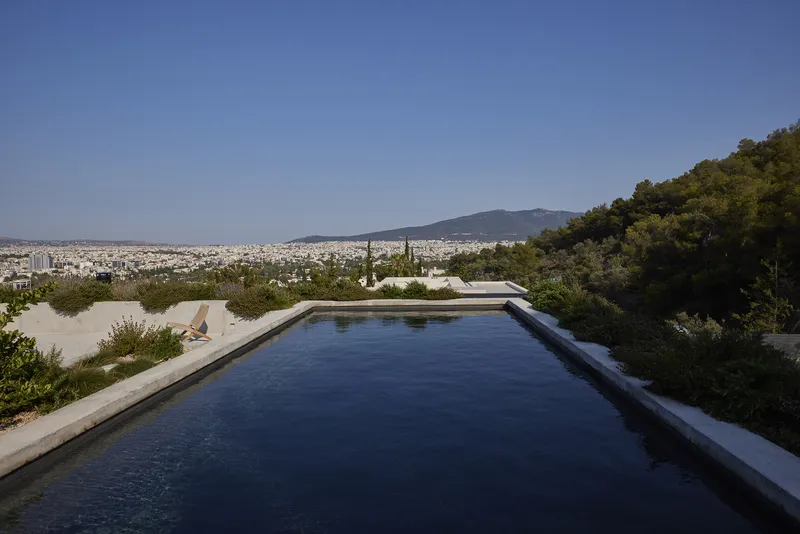 Concrete-edged infinity pool overlooking the cityscape with hills in the distance under clear skies