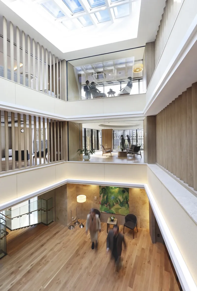 Multi-story atrium with vertical timber slat screens, overlapping balconies and skylight above people walking below