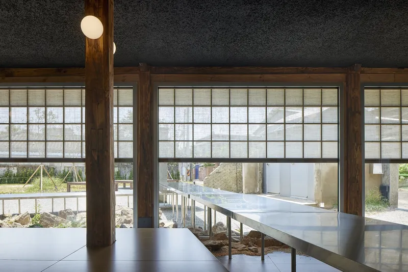 Interior view through timber-framed shoji screens with elevated steel table bridging exposed earth beneath