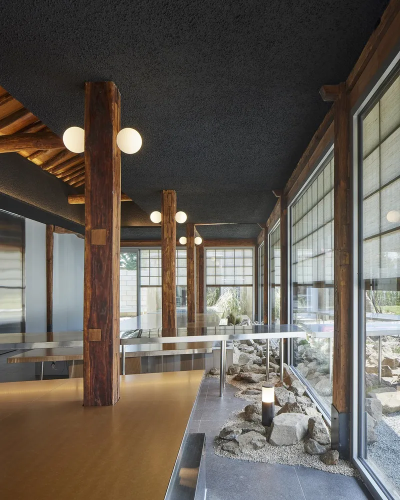 Interior with timber columns, exposed rafters, and a rock garden visible through gridded glass panels