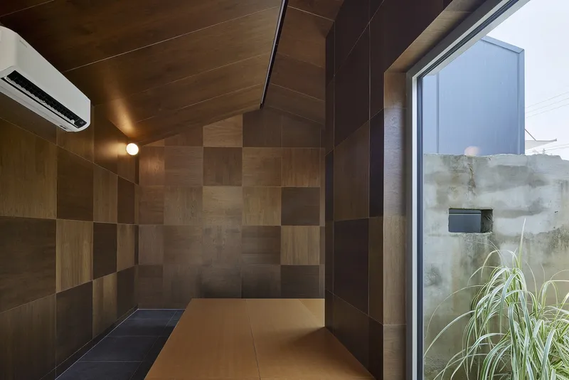 Room with chequered wood paneling on walls and ceiling and view to a concrete wall
