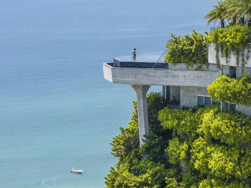Cantilevered concrete terrace with planted balconies and a figure looking toward the turquoise water