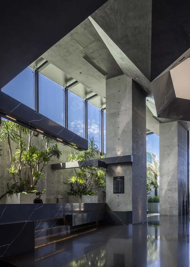 Double-height lobby with cast-in-place concrete columns, clerestory windows, and planted interior courtyard