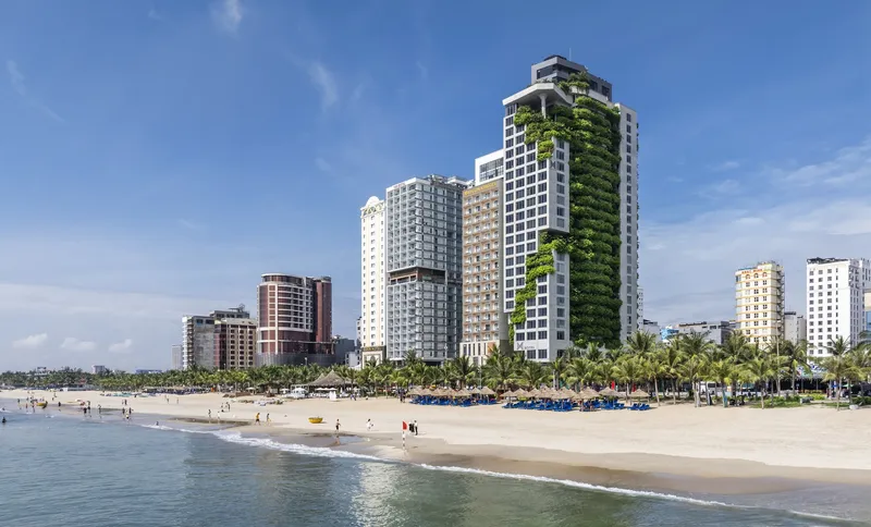 Beachfront view of residential tower with cascading vertical gardens under a clear blue sky